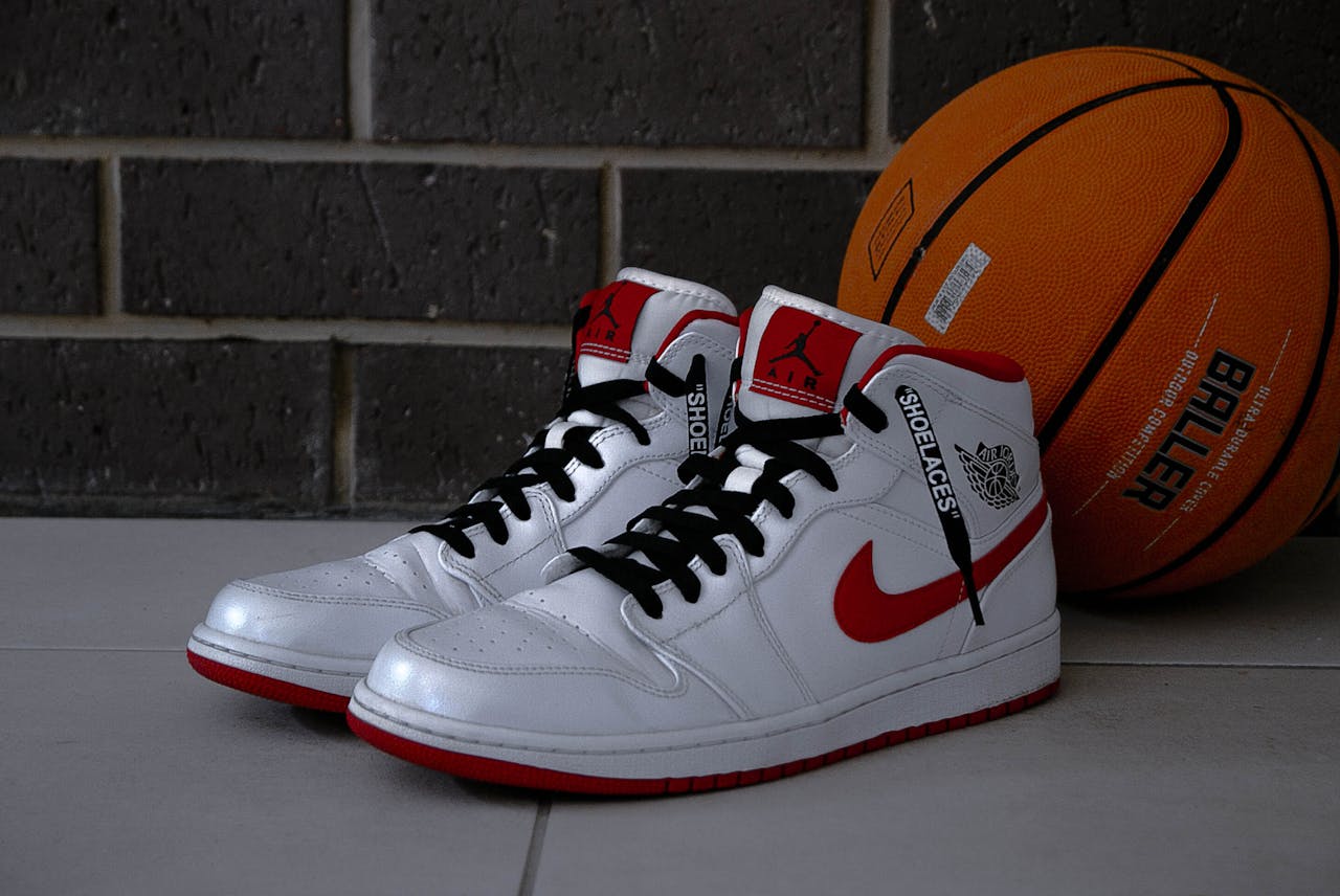 White and red basketball sneakers with an orange basketball on tiled floor.